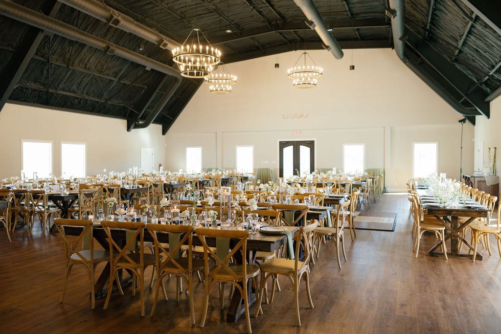 Wide view of the reception hall with farm tables and chandeliers